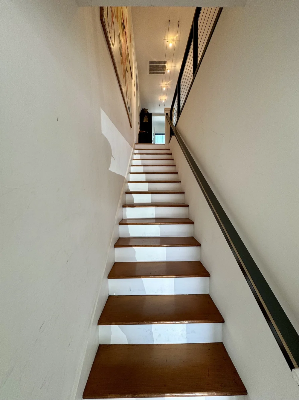 Indoor staircase with wooden steps and metal handrail leading to a bright upper floor