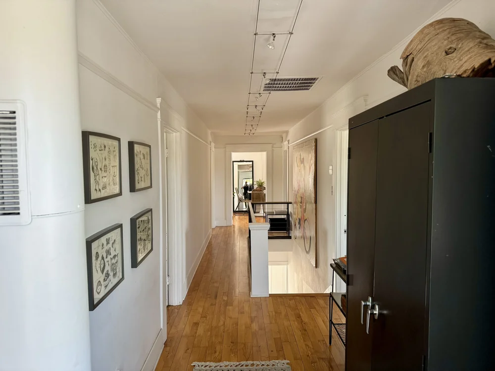 Interior hallway with hardwood floors, framed artwork, and a black storage cabinet