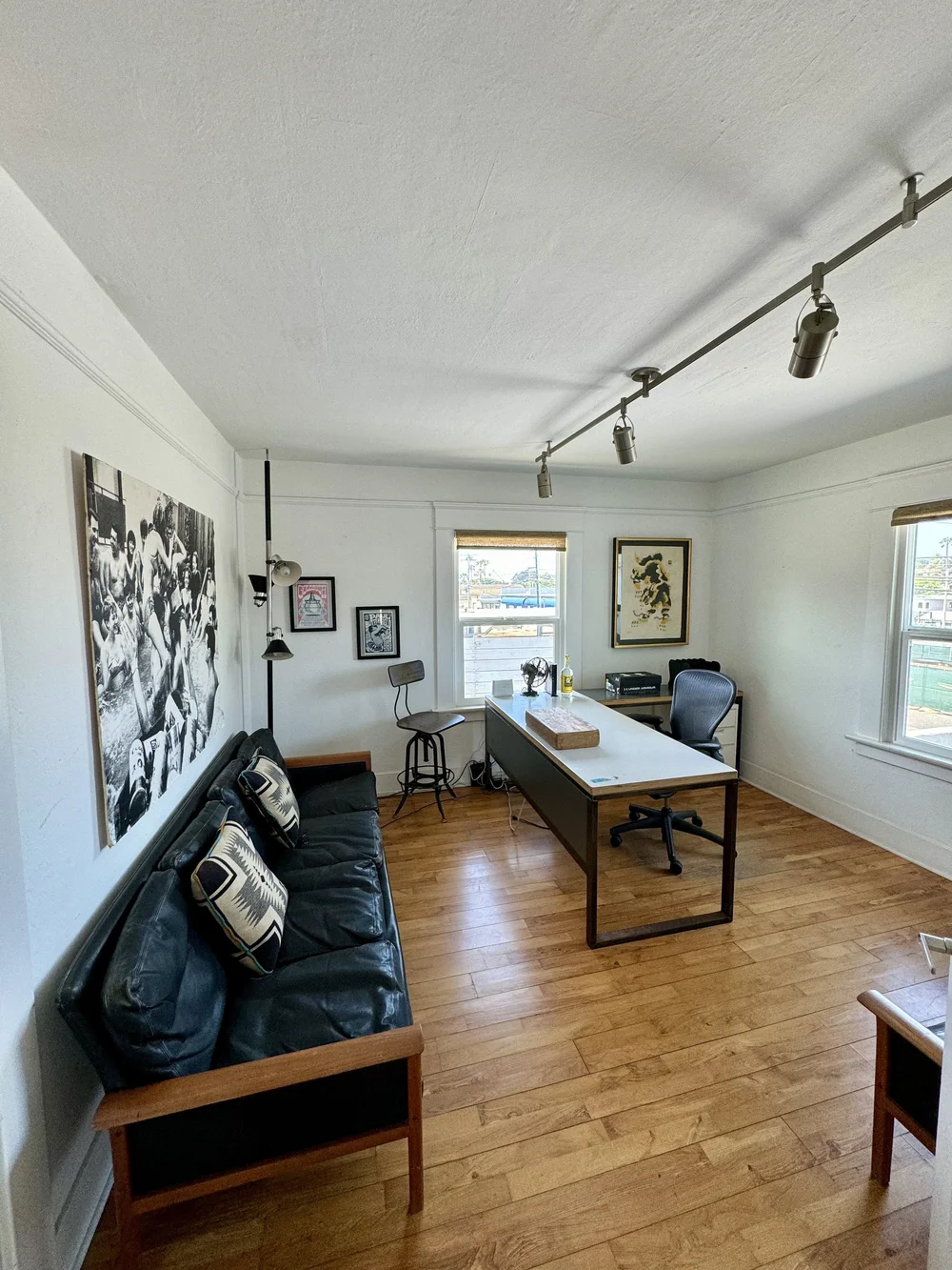 Home office with a black leather sofa, wooden desk, office chair, and framed wall art