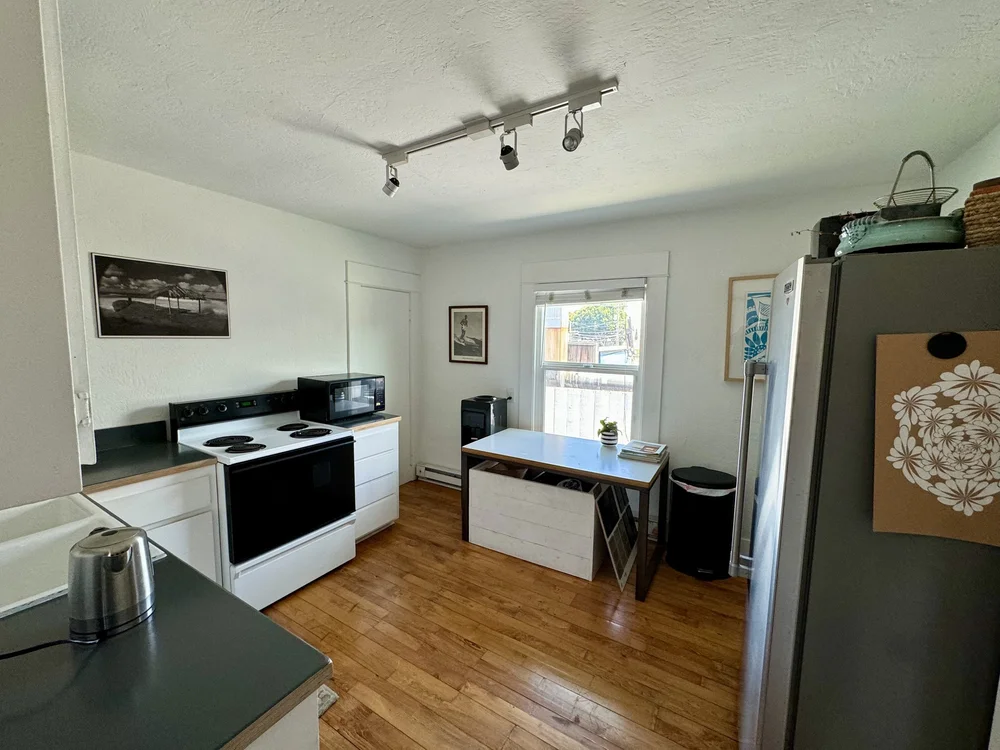 Shared kitchen with white cabinets, stove, microwave, and a small table
