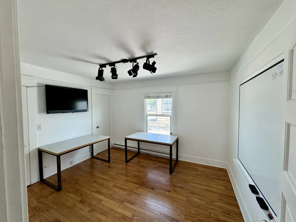 Meeting room with a mounted flat-screen TV, two desks, and spotlight ceiling fixture