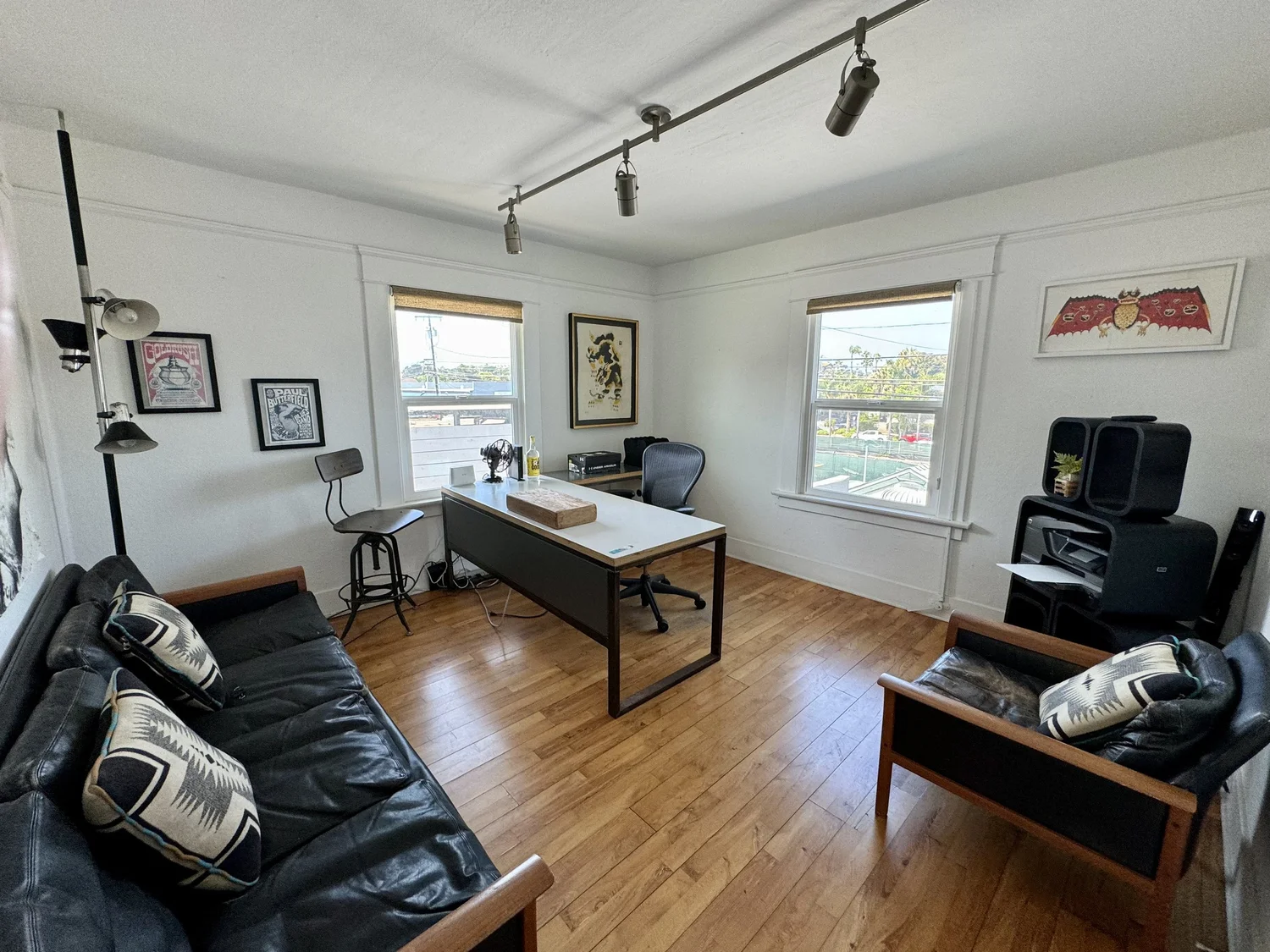 A private office with black leather sofas, a desk with an office chair, and large windows with ocean views